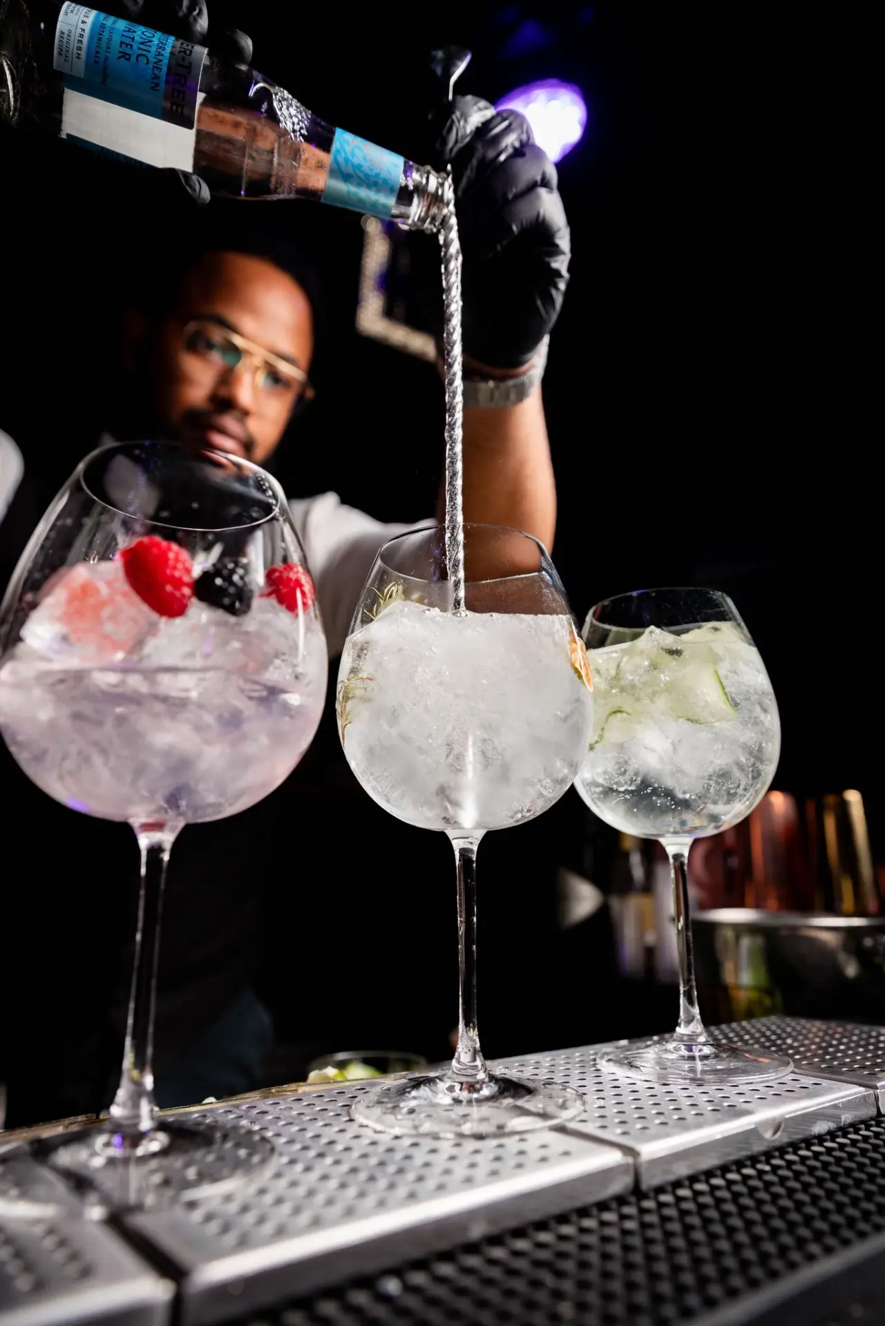 Bartender pouring tonic into gin glasses garnished with berries