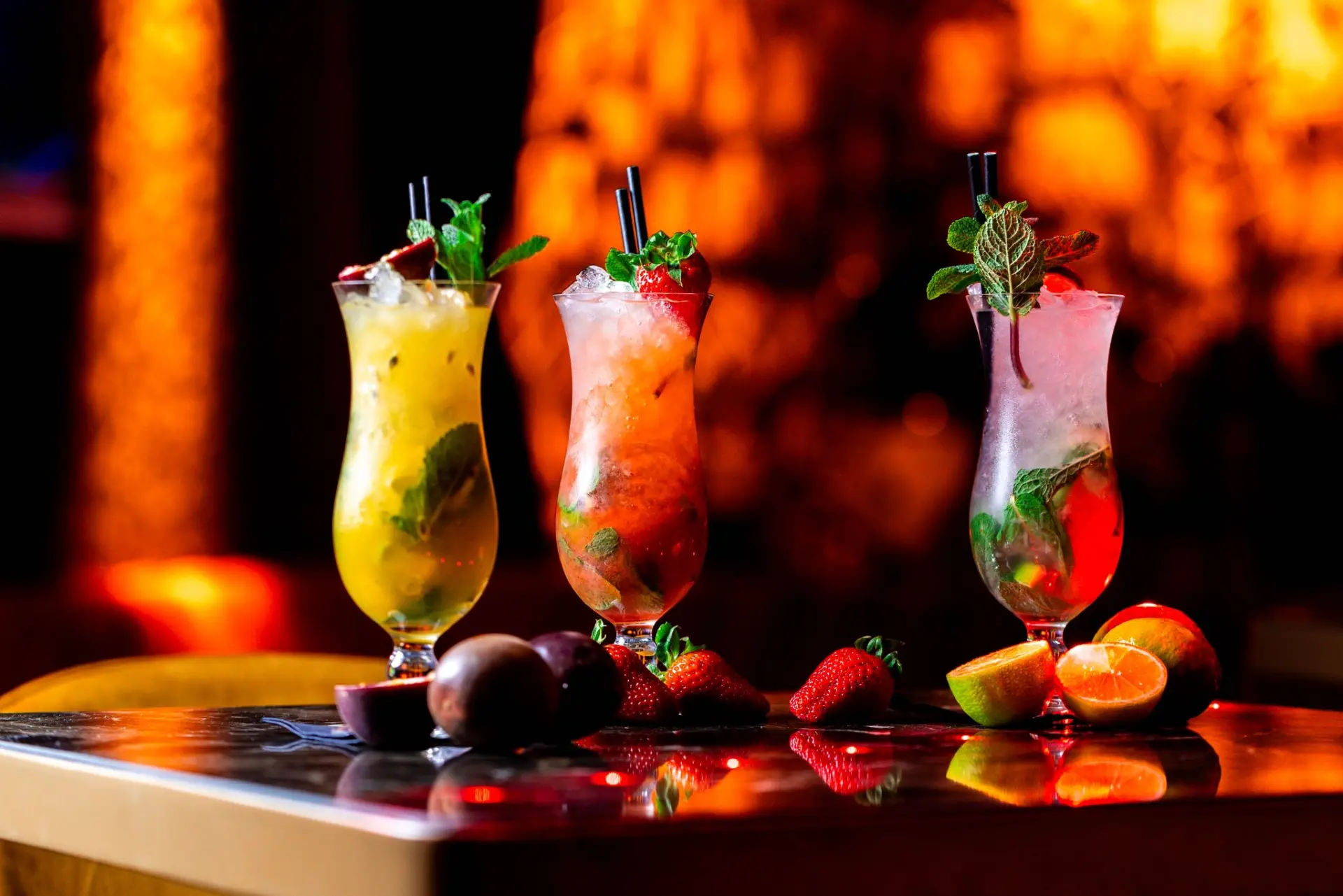 Three cocktails on a bar with warm amber lighting behind
